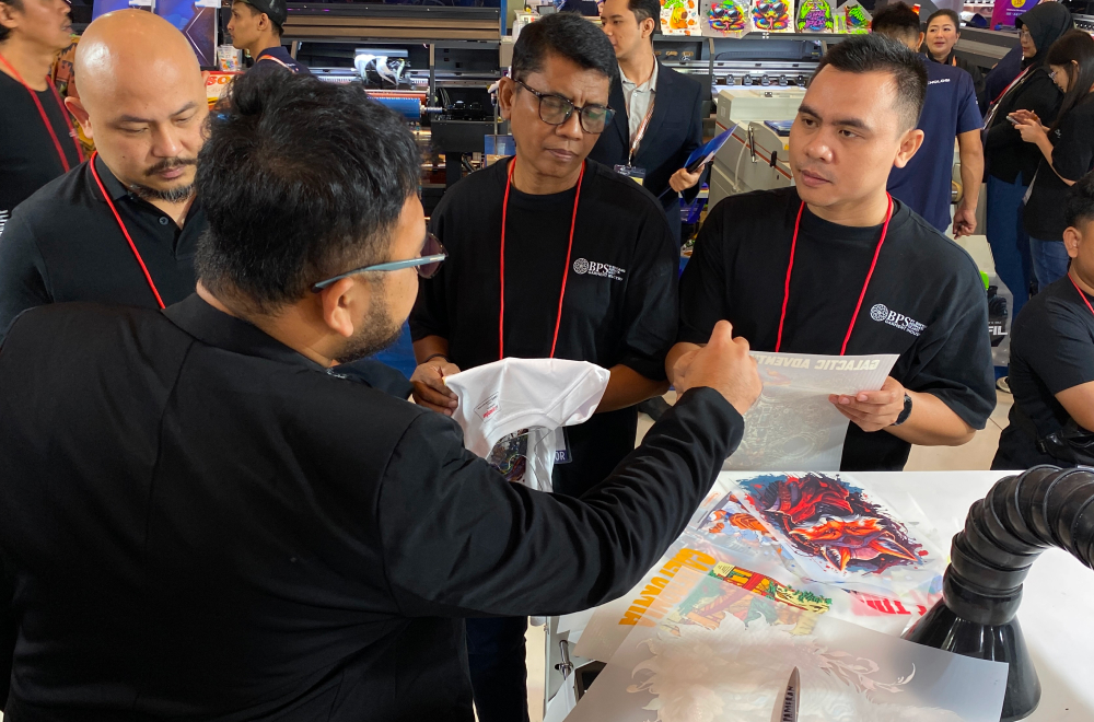 Seorang Pengunjung Sedang Berdiskusi Dengan Vendor Mengenai Hasil Cetakan Dtf Di Pameran Digital Printing.