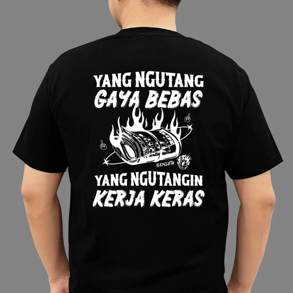 Seseorang Mengenakan Kaos Hitam Dengan Tulisan Humor Bertema Sosial “Yang Ngutang Gaya Bebas, Yang Ngutangin Kerja Keras” Berdesain Ilustrasi Uang Terbakar.